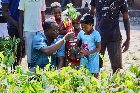 Vater übergibt Sohn Baumsetzling in Mosambique